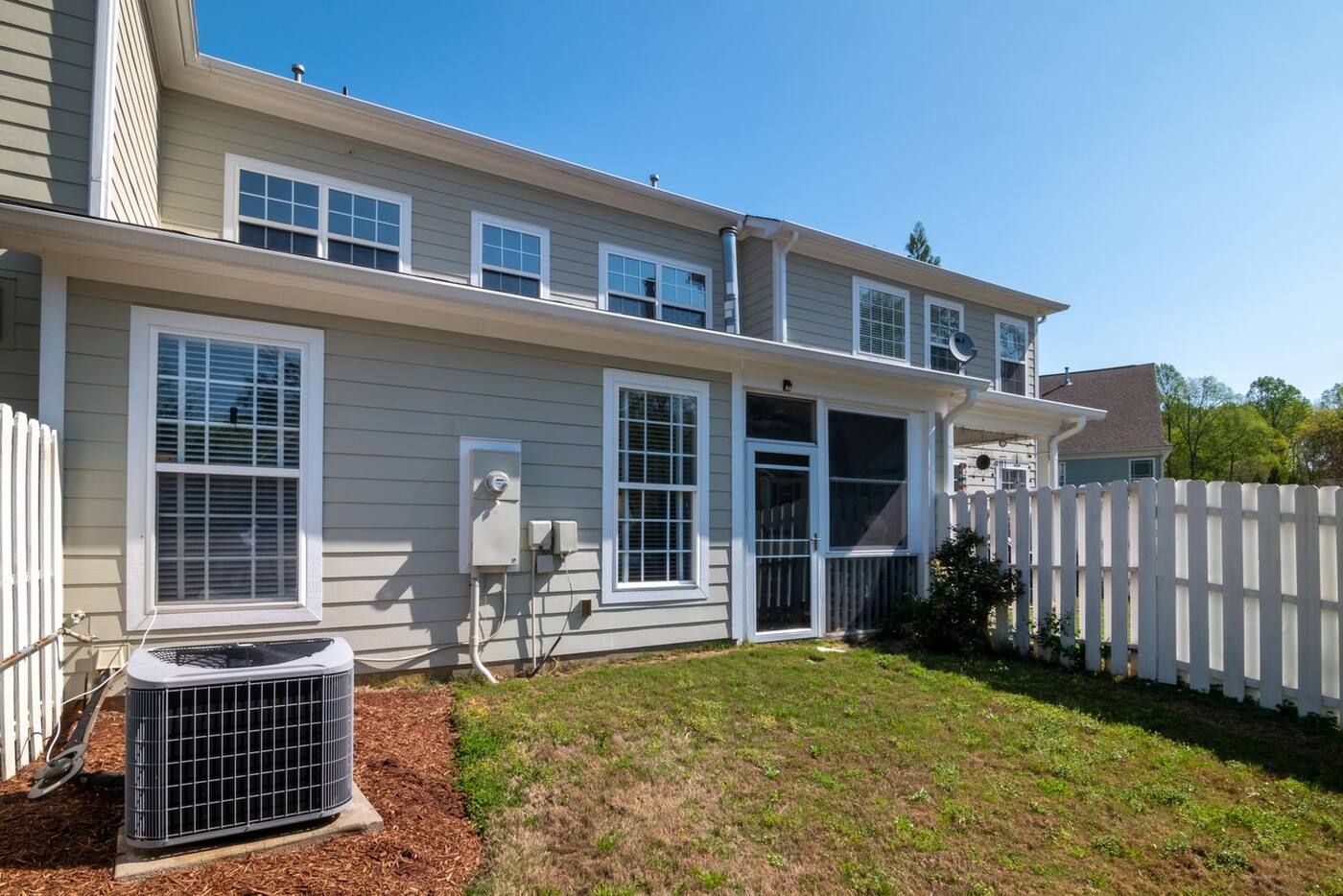 An outdoor AC unit on a pad behind a two-story townhouse