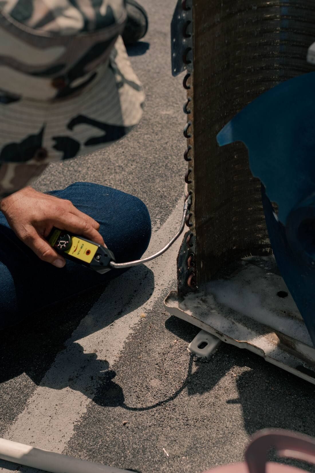 A technician holding a refrigerant leak detector with its probe at the coil of an opened outdoor unit