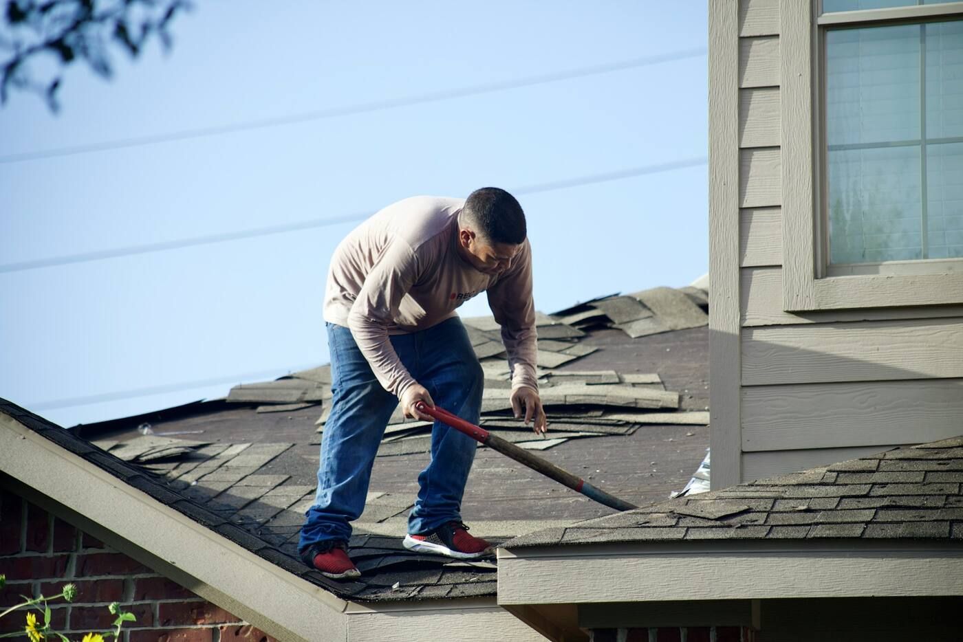 Before: a roofer tearing worn shingles off a house