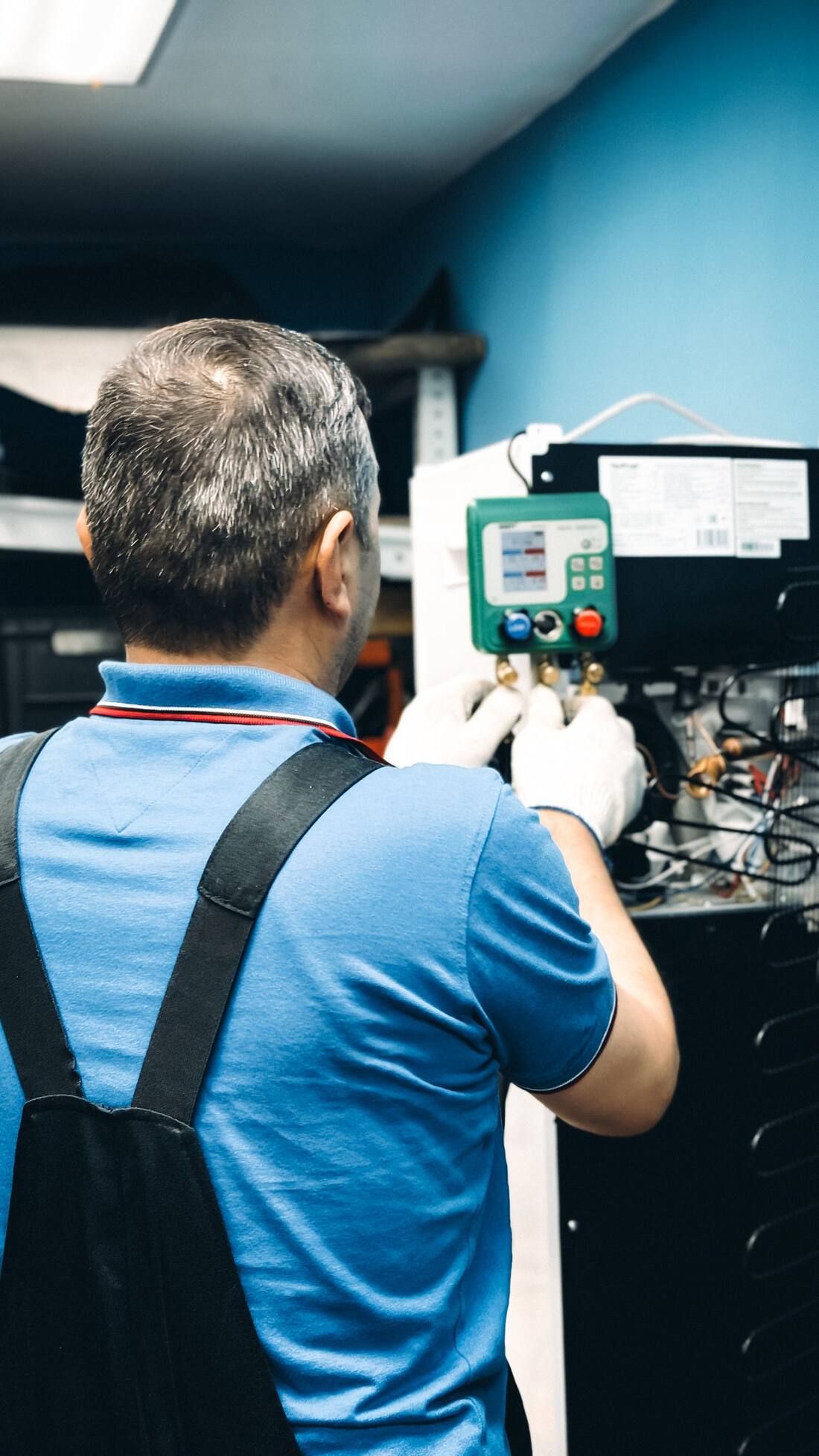 A technician, seen from behind, with digital refrigerant gauges hooked to a unit